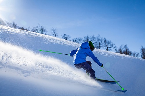 Skier wearing a blue jacket skiing down a mountain, spraying snow.