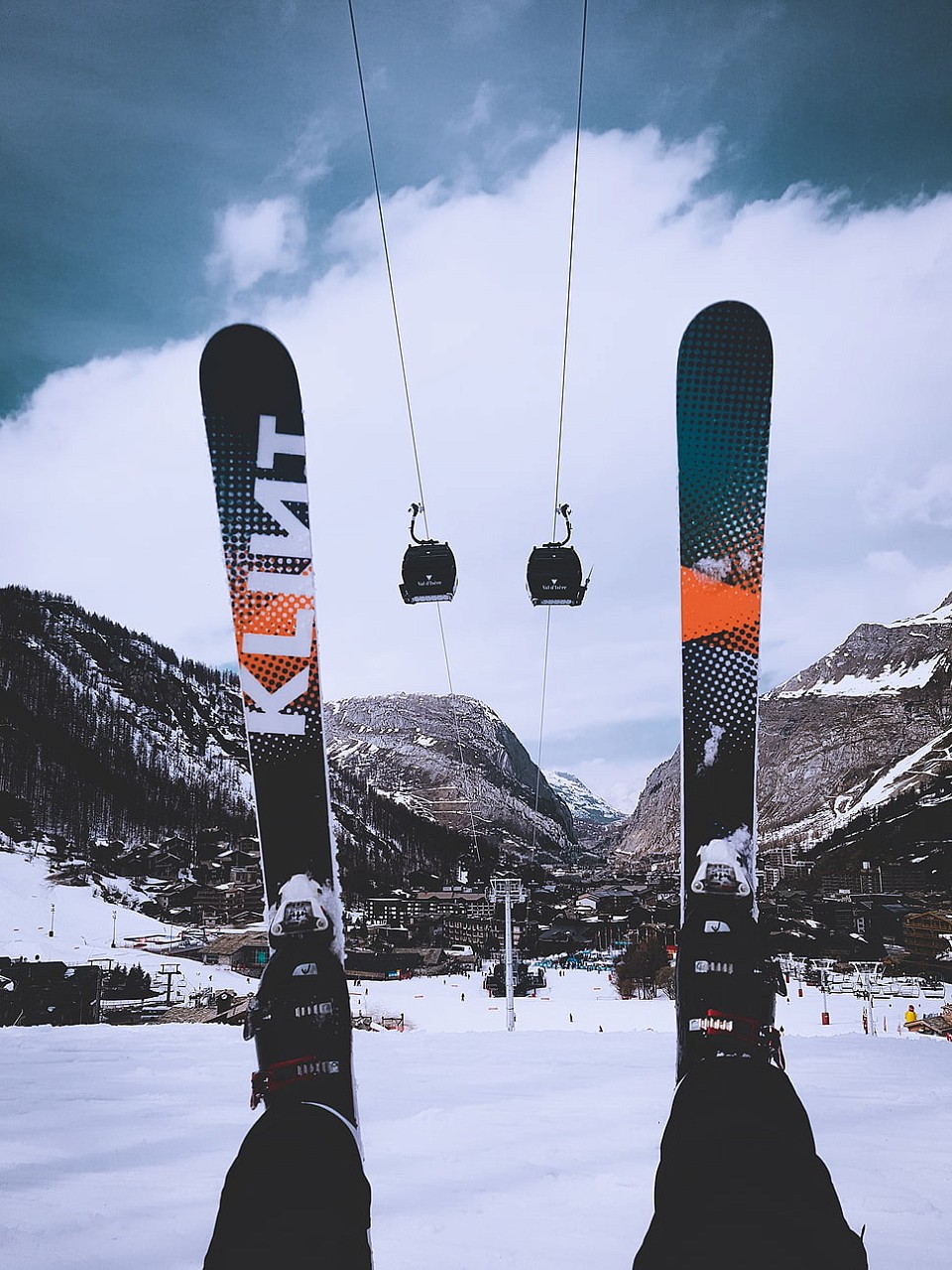 A pair of skis raised in the air, in the background is a ski lift, mountains and clear blue sky
