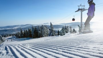 A person skiing down a freshly groomed ski slope, there are trees and snowy peaks in the background