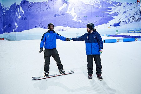 two people in blue Chill Factor<sup>e</sup> jackets fist bumping, one is stood on a snowboard