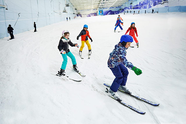 group of kids on a skiing lesson skiing down the ski slope all in their ski clothing