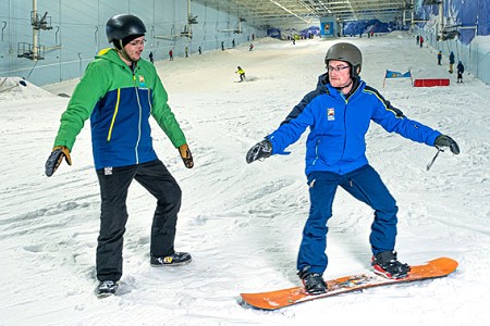 A snowboarder receiving a snowboarding lesson from a chill factore instructor at the indoor slope