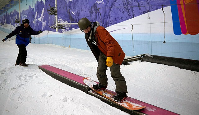 a person trying to perform a trick whilst stood on an orange snowbaord in their red jacket