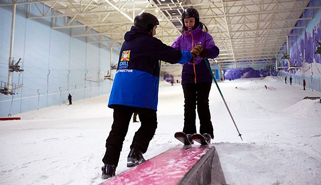 chill factore instructor in a blue jacket helping a woman in a purple jacket on her skiing lesson