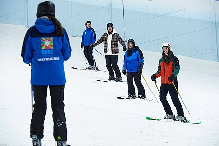 Group of skiers lined up on the main slope looking to an instructor in the foreground.