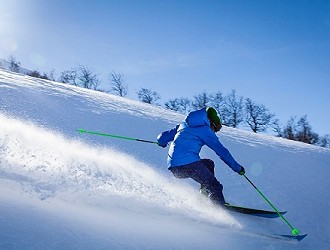 Skier going down an outdoor snow slope, wearing a blue coat and black ski pants