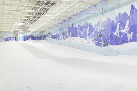 An indoor ski slope with snow on the ground. There are blue mountains painted on the blue walls.
