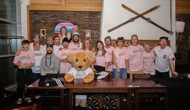 a group of people stood behind a table in pink t shirts with a person in a bear costume