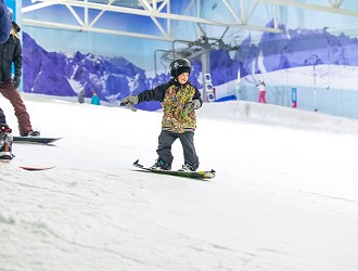 young kid in a multicolour coat and black helmet snowboarding on the slope
