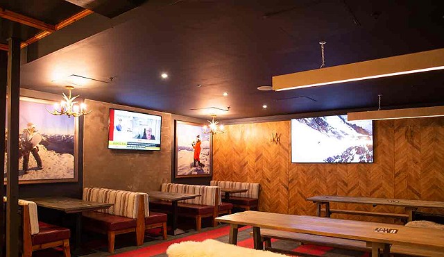 A wooden lodge style restaurant with bench seats, the tv on the wall is showing snowy peaks