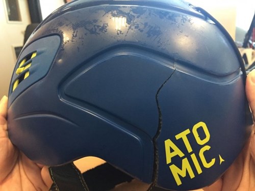 A close up picture of two hands holding a broken blue and yellow atomic ski helmet with ventilation