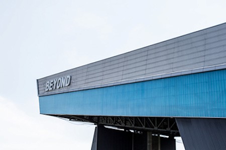 Top of a blue building with the logo at the edge, in the background is a grey sky.