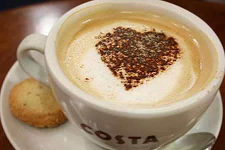 Costa Coffee cup with a coffee in it and a love heart on the top, with a biscuit on the side