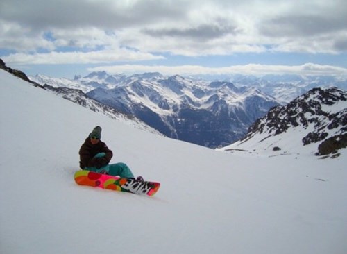 person sat on the snow with their snowboard and the snowy mountains in the background