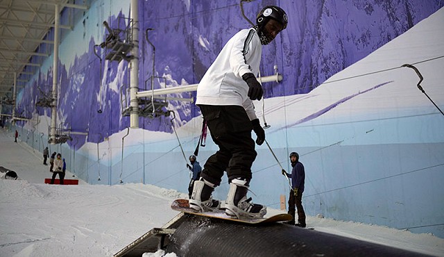 person wearing white and a black helmet performing a snowboarding trick in chill factore