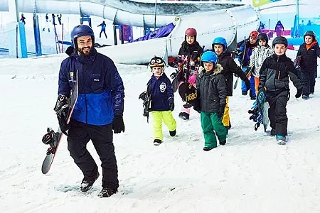 Group of children being led to the slopes for a snowboard lesson by their instructor