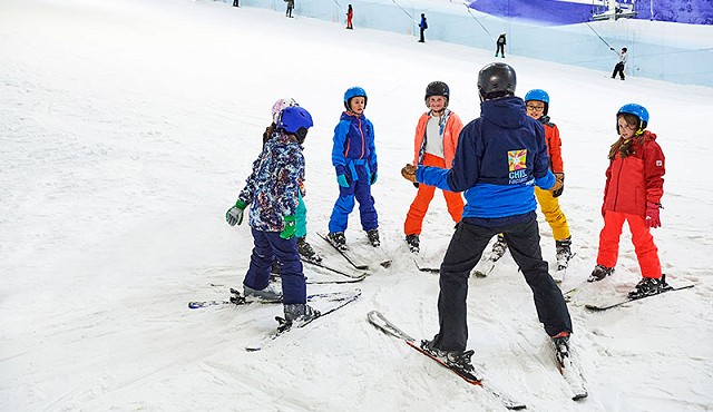 group of kids on a skiing lesson stood around in a circle listening to a chill factore instructor