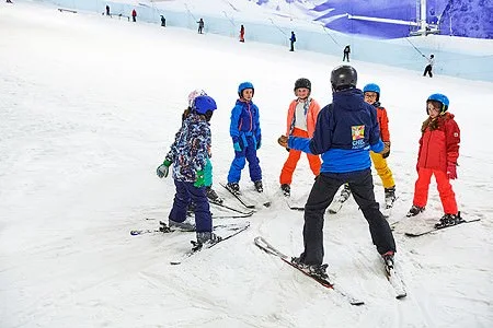Group of children wearing ski clothing on skis, gathered around their ski instructor on the main slope at Chill Factor<sup>e</sup>