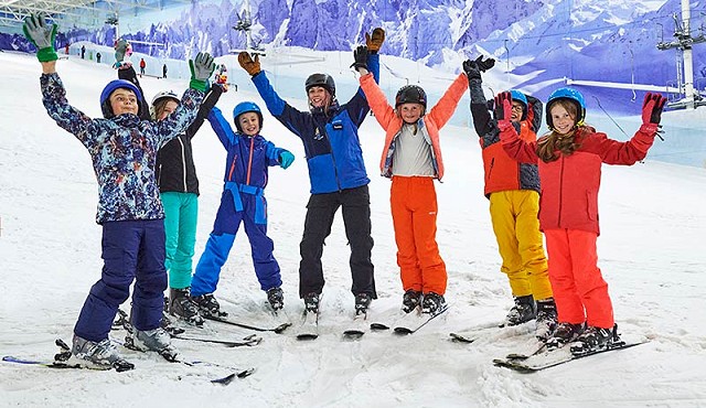group of kids on a skiing lesson all stood in a line with their hands raised in the air