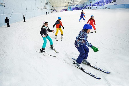 Group of junior skiers in bright ski clothing skiing down an indoor snow slope.
