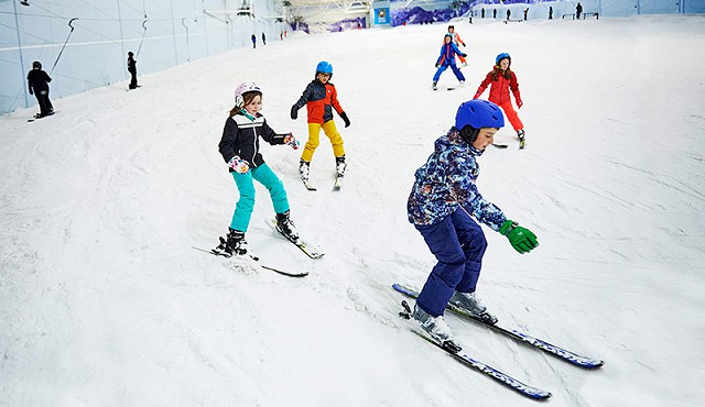 group of kids on a skiing lesson skiing down the ski slope all in their ski clothing