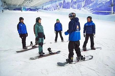 Shot of group of snowboarders stood on snow slope listening to some feedback from their instructor.