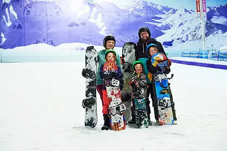 A family group of snowboarders posing for a photo on the beginner slope at Chill Factor<sup>e</sup>