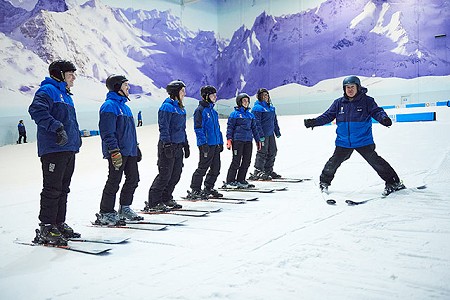 Group of adult skiers on the beginner slope at Chill Factor<sup>e</sup> stood listening to their instructor.