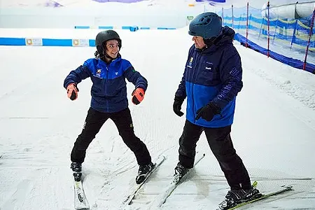 Skier in snow plough pose getting some tips from their instructor