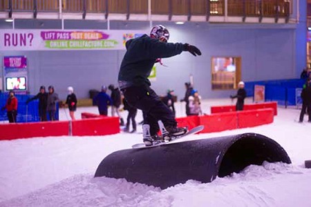 A snowboarder performing a trick on a plastic pipe at Chill Factor<sup>e</sup> indoor ski slope