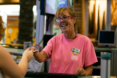 Woman in pink t shirt, she is smiling and handing something to a person infront of her.