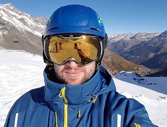 a man out on the ski slopes with a blue coat and hood up with golden skiing goggles