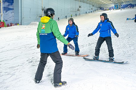 two people on a snowboarding lesson trying to balance with the help of an instructor