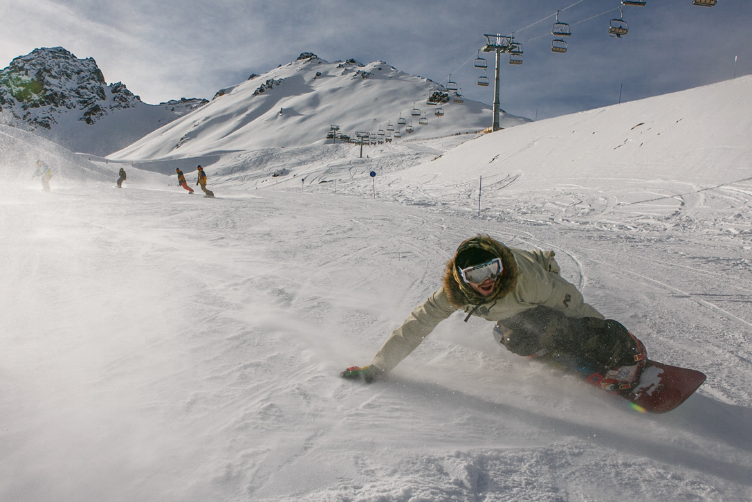 a person snowboarding down some snowy mountains with their arm outstretched to change direction