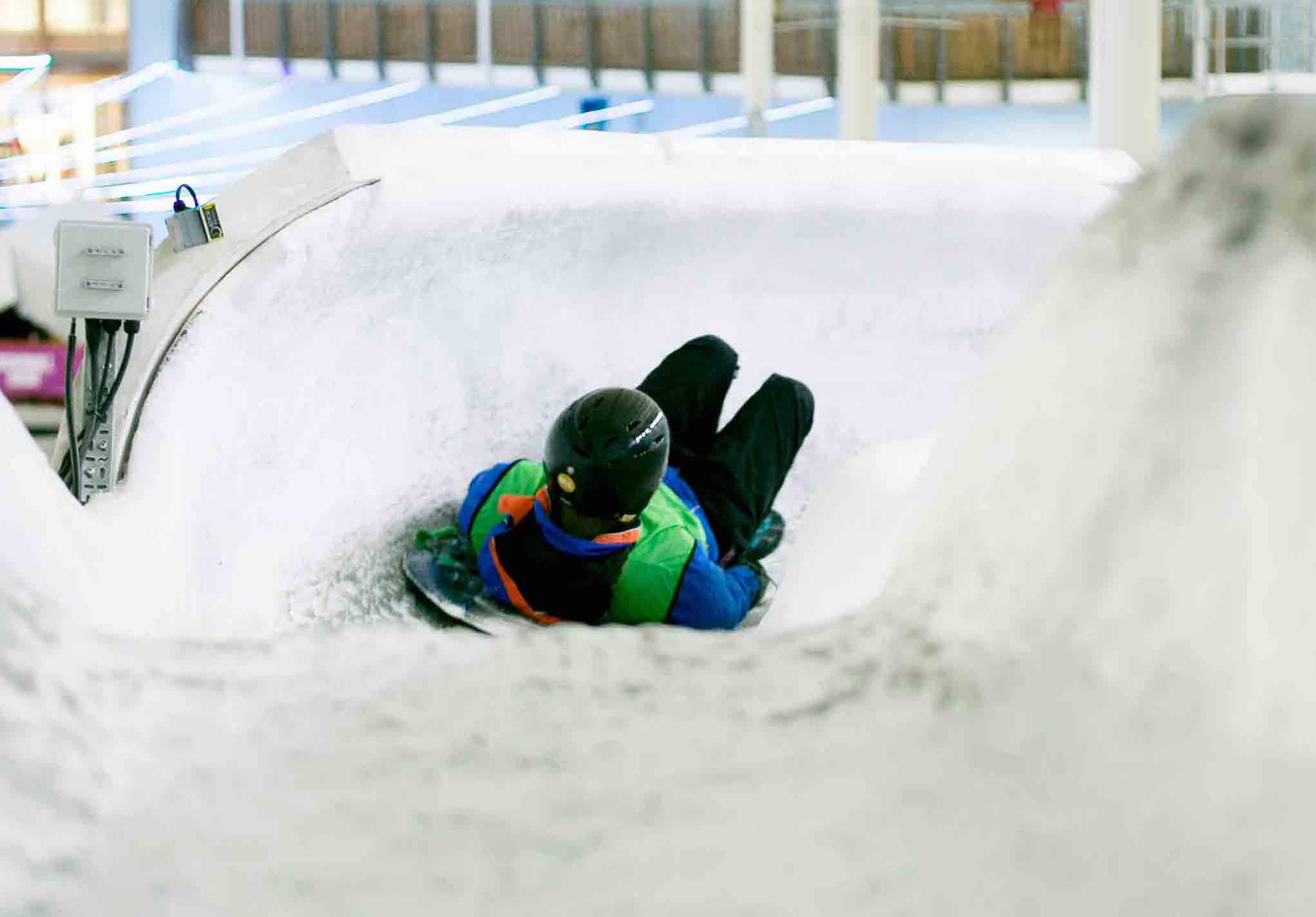 a person going down the ice slide in their blue and green jacket and black helmet