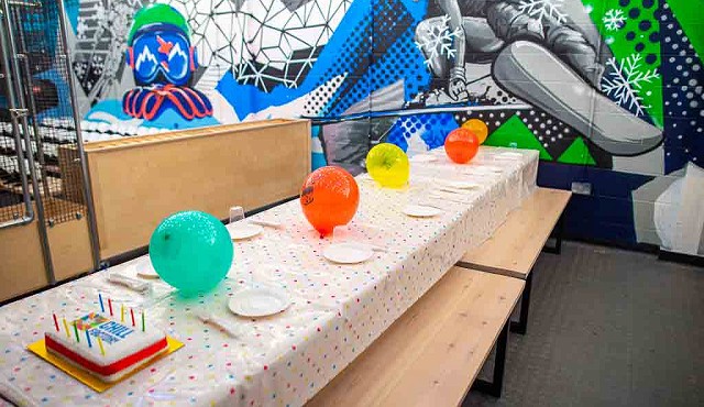 a table with a spotty table cover, baloons, a birthday cake and paper plates set ready for a party