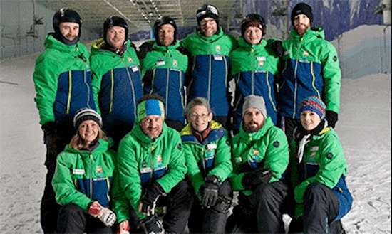 a group of eleven people stood with smiles on their faces all wearing the same green and blue coats