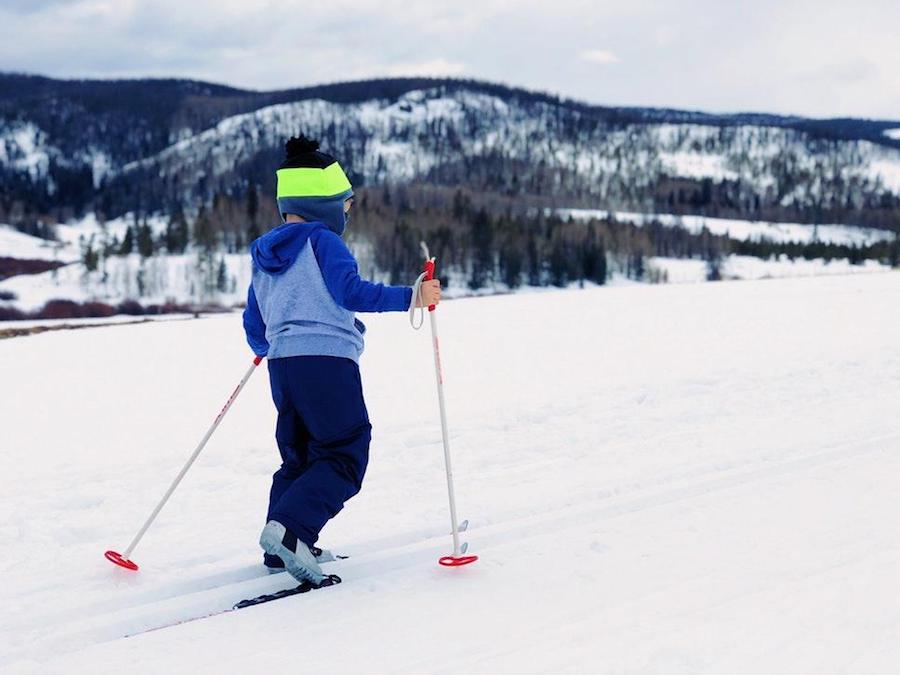 Child skiing with ski poles outdoors surrounded by snowy mountains