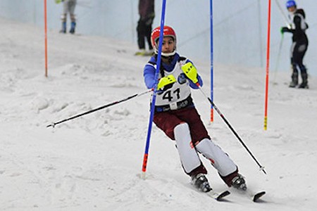 Young person skiing around obstacles in the snow, they are wearing a red helmet and yellow gloves.