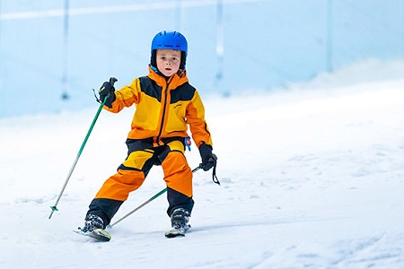 Young boy in yellow ski clothing sking to camera