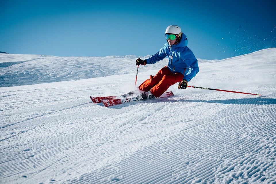 person skiing in a snowy location wearing a blue jacket and orange pants