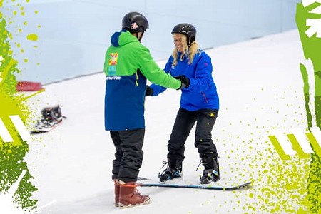 Woman receiving a snowboarding lesson from an instructor, she is wearing a blue jacket and trousers.