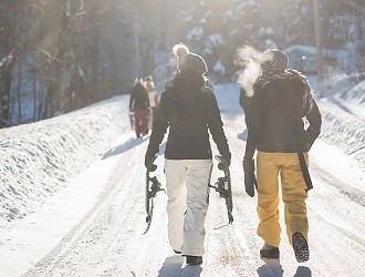 Two people in snow clothing, walking along the road, they are wearing white and yellow trousers