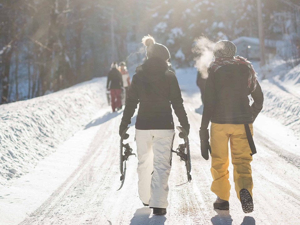 Two people in snow clothing, walking along the road, they are wearing white and yellow trousers