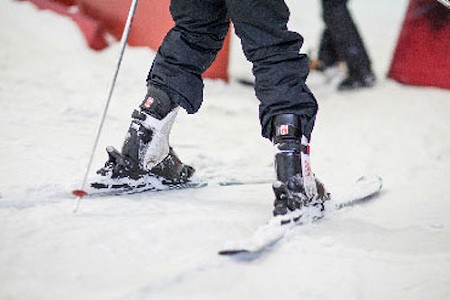 Close up of an individuals legs whilst skiing, they are wearing black trousers and ski boots.