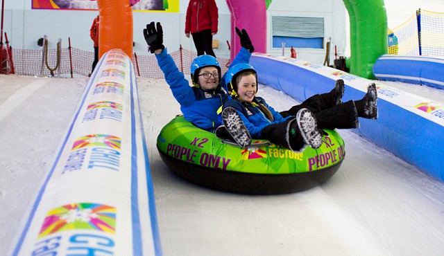 Two young people sliding downhill on an inflatable ring on the snow, they are both smiling.
