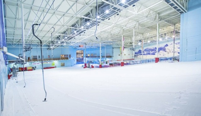 An empty ski lift on an indoor ski slope, there is snow on the ground. The indoor walls are blue.
