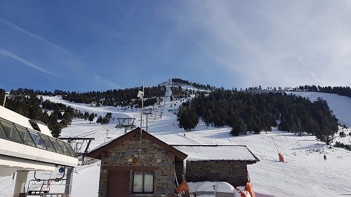 A ski village filled with snow, in the background is a mountain range with snowy peaks and trees