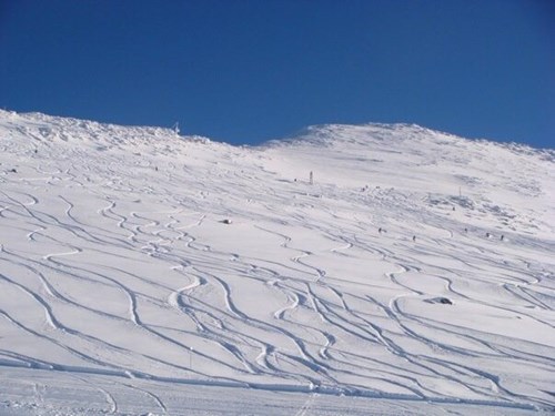 A snowy mountain peak with blue sky in the background, there are ski tracks in the snow