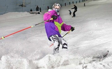 A person skiing in bright coloured clothing, flicking up snow as they turn the corner